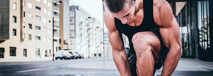 A male runner kneeling down to tie his shoelaces